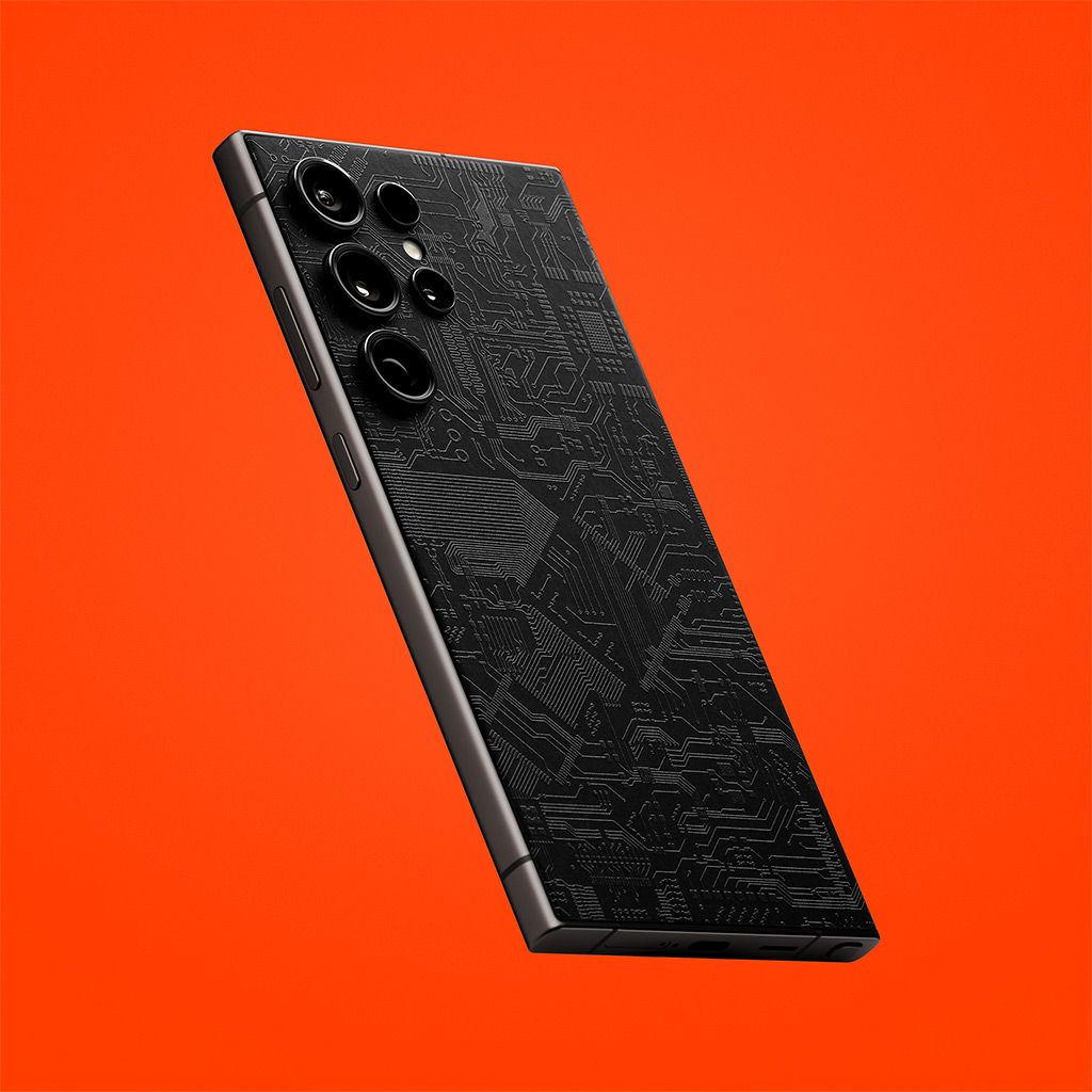 An S24 Ultra seen from the back. The device has our Dark Circuit Skin on it, showing the black tone of the material with an orange backdrop.