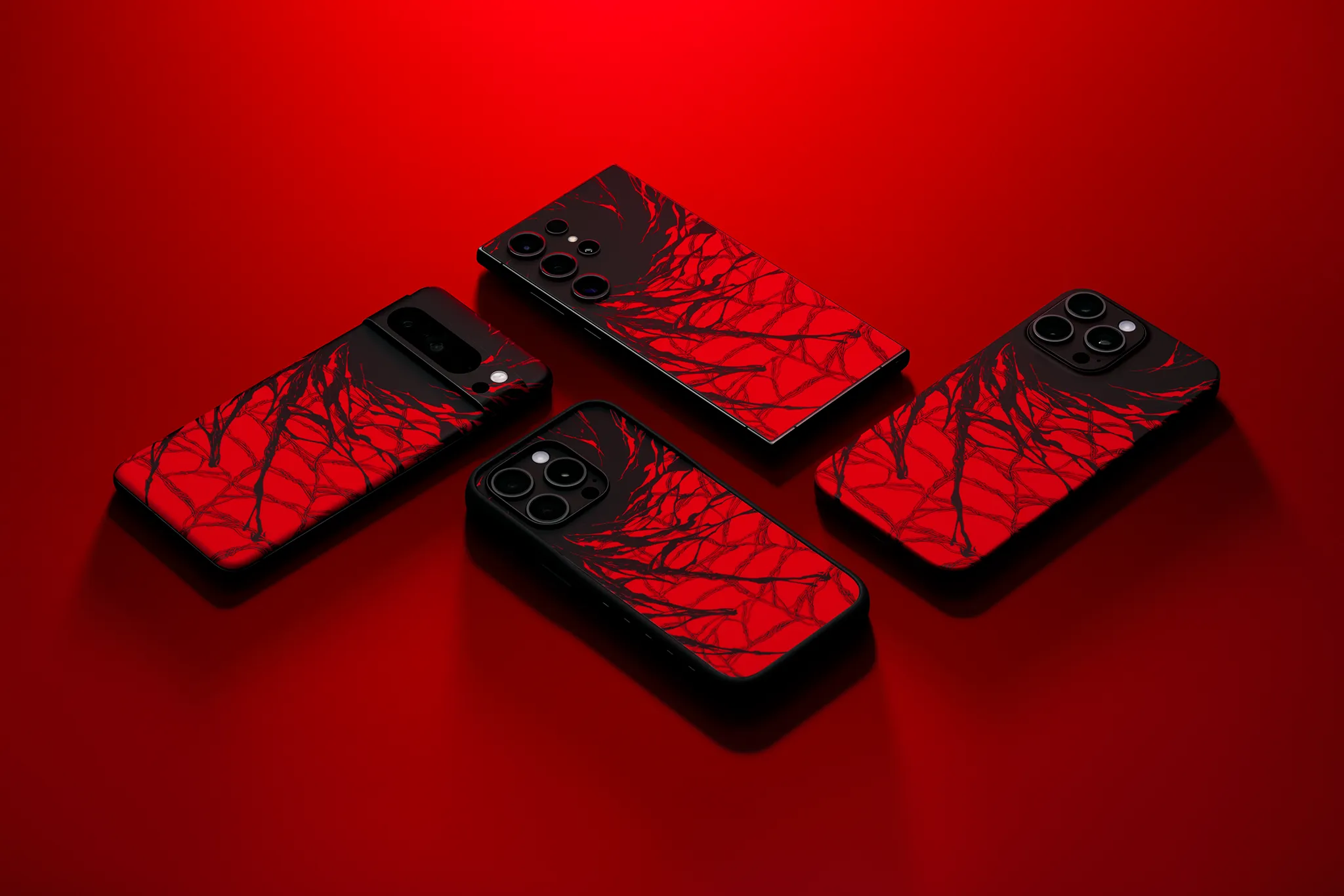 A Pixel 8 Pro, a Samsung S24 Ultra, and two iPhone 14 Pro Maxes, all face down against a red backdrop. One of the iPhones has our Grip Case on it, and all of the devices have our Carnage Skin applied.