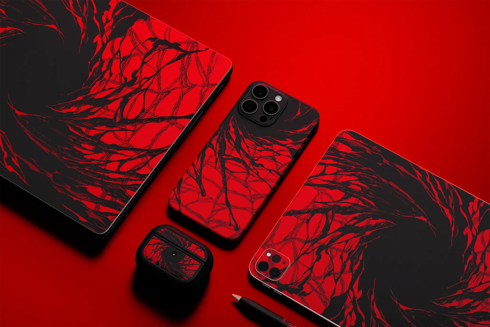 A MacBook, an iPhone 14 Pro Max, an iPad, an Apple Pencil, and an AirPods Case, all against a red backdrop and with our Carnage Skin applied. The iPhone, and iPad are face-down, while the MacBook and AirPods have their front face visible.