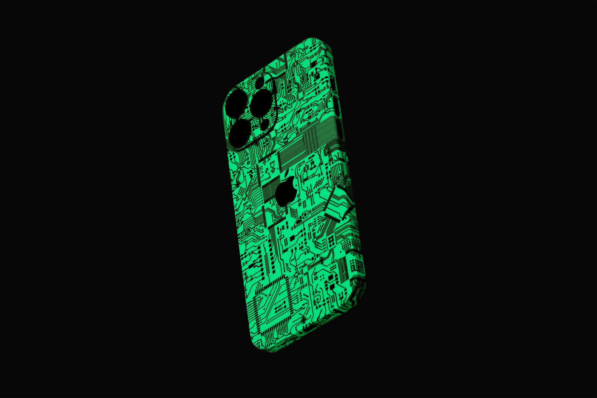 An iPhone 16 Pro Max at an angle, seen from the back. The device has our Circuit Board Skin on it, showing the fluorescent green tone of the material on a black background.